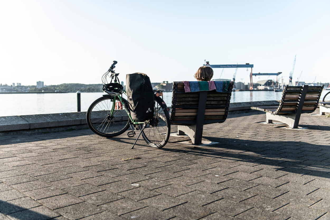 Eine Radfahrerin pausiert an der Kiellinie in Kiel.